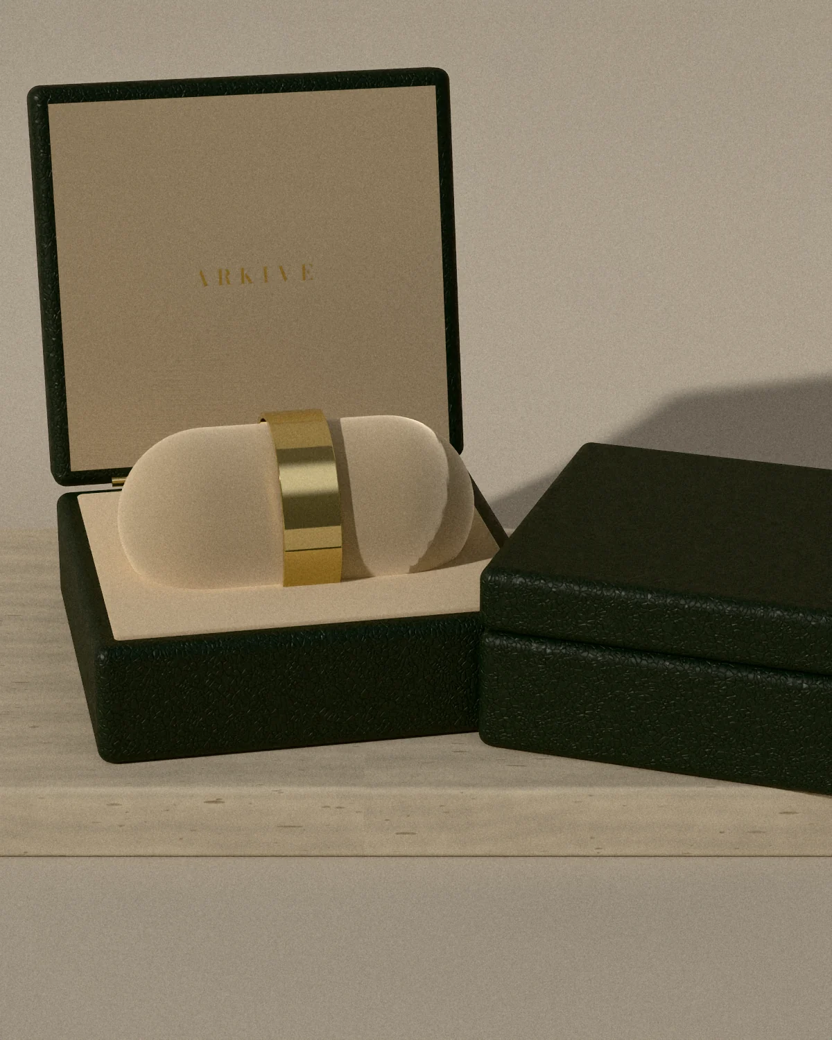 An open green leather case holding a brass cuff on a suede cushion, a closed case beside it on travertine