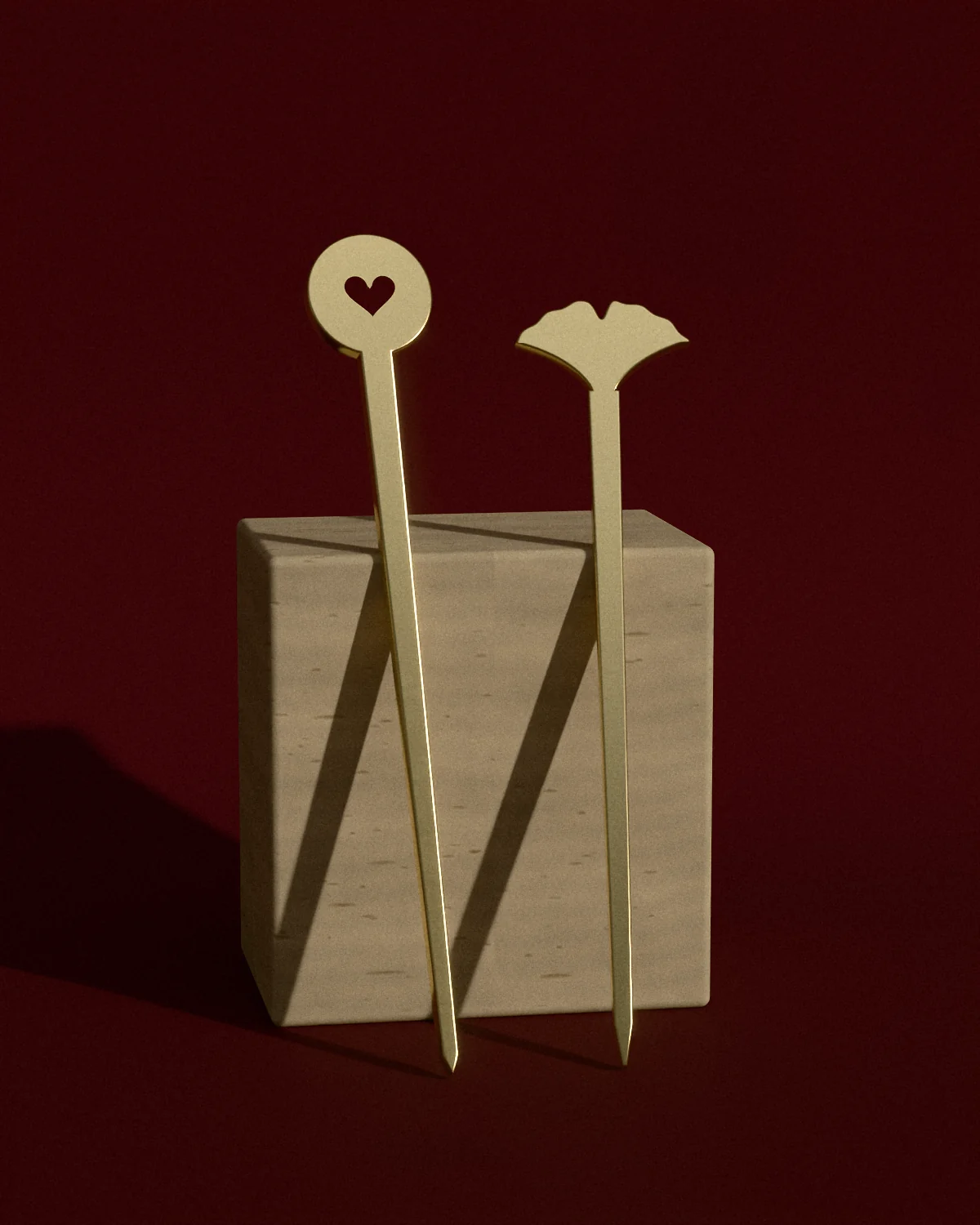 Two brass hair sticks resting on stepped travertine against oxblood paper